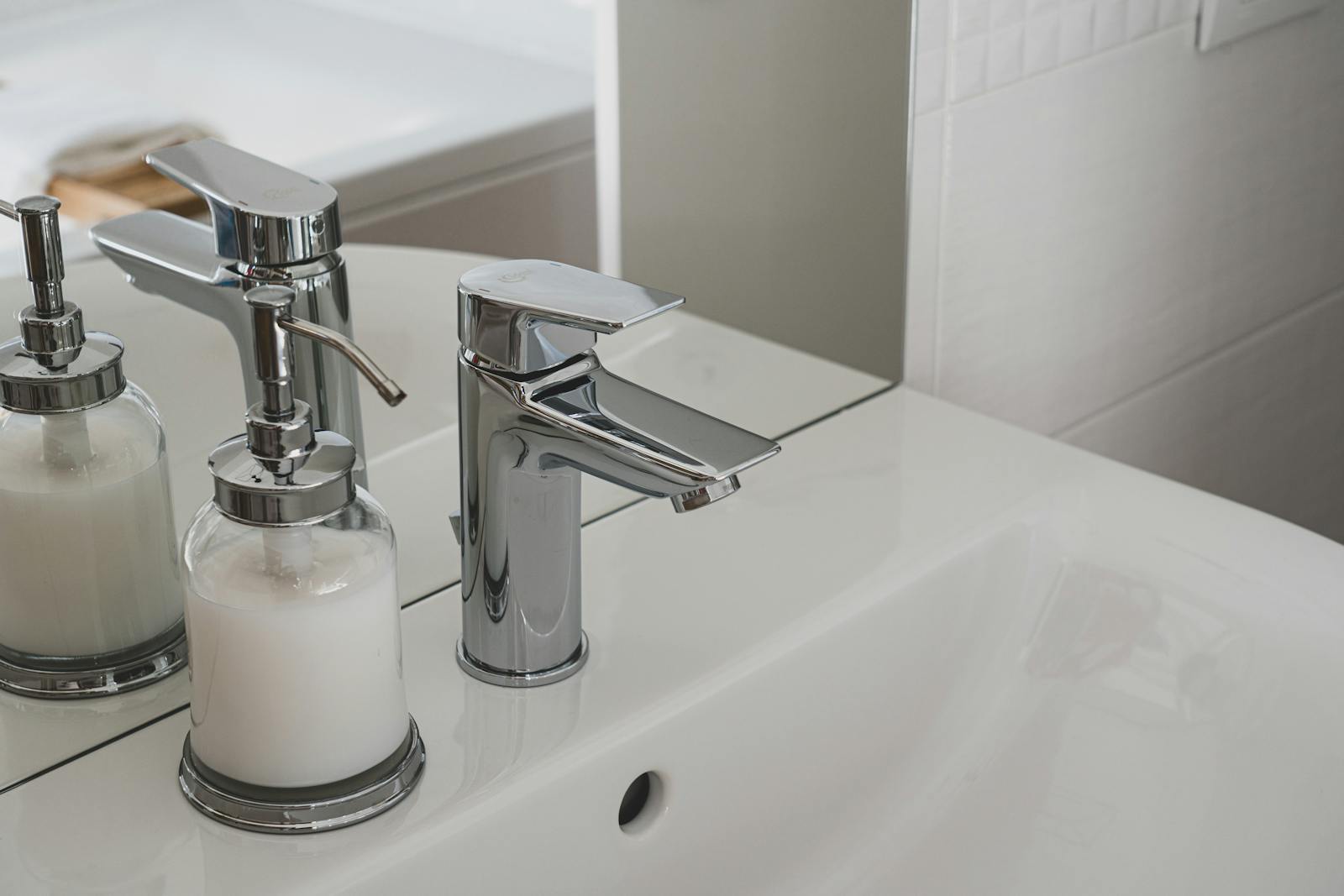 A sleek chrome faucet and soap dispenser on a pristine white sink in a modern bathroom setting.