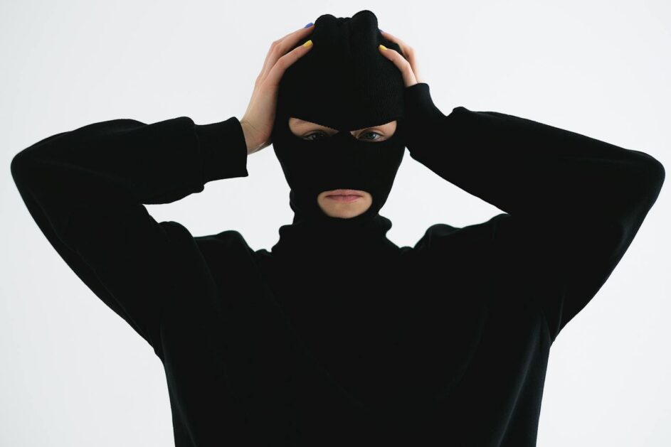 A person in a black balaclava with hands on head creates a mysterious and suspenseful vibe.
