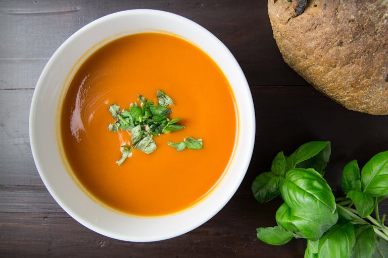 Delicious homemade tomato soup served with basil leaves and rustic bread.