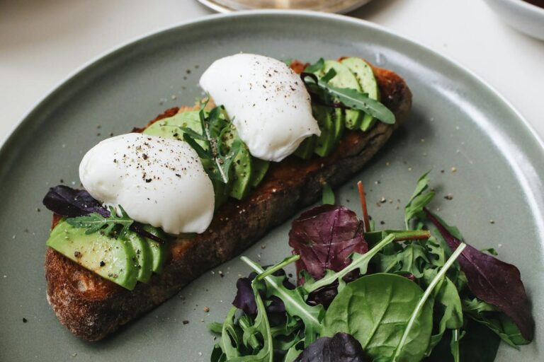 Gourmet avocado toast topped with poached eggs and fresh greens on a ceramic plate.