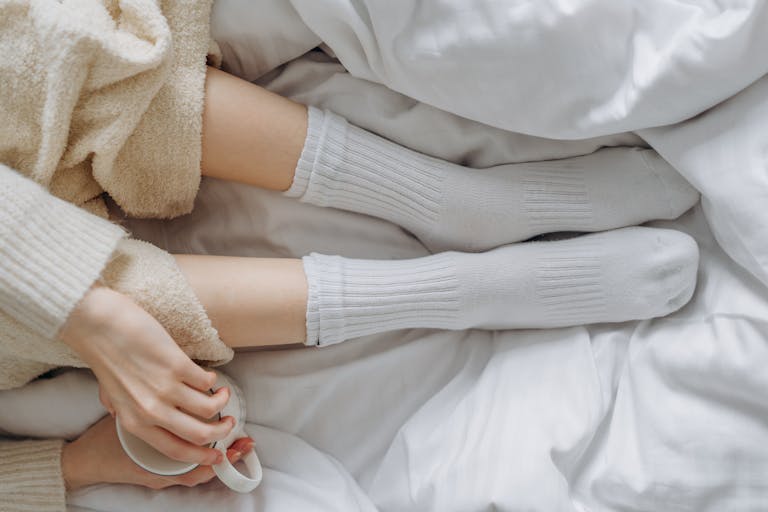 Relaxing indoors wrapped in white linens and warm clothing, enjoying a soothing moment with a cup.