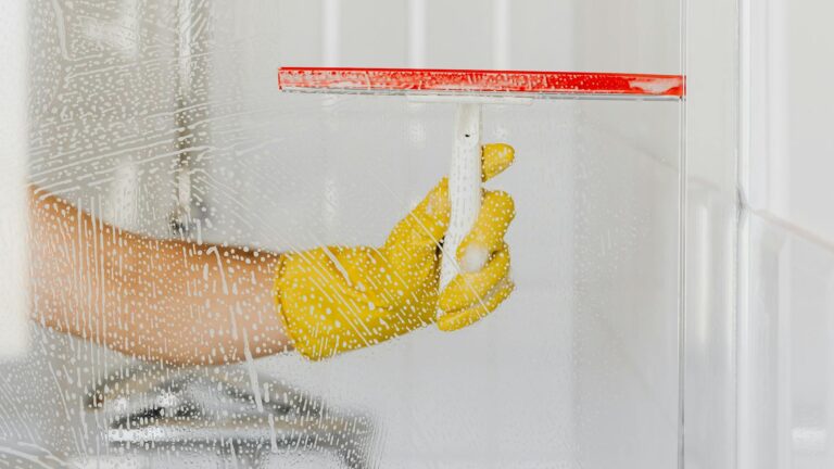 Osoba myjąca szybę prysznicową w klasyczny sposób