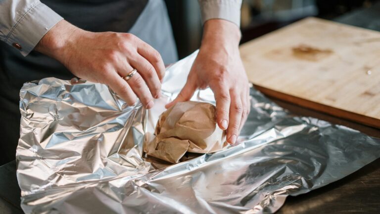 Close-up of a chef's hands wrapping food ingredients in foil for cooking.