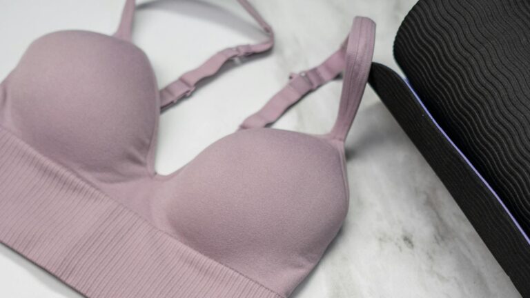 Pastel pink sports bra, sneakers, and yoga mat with earphones on marble.