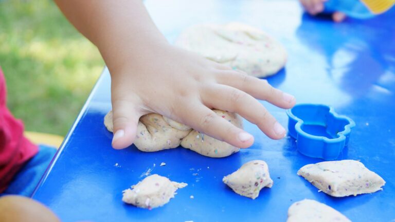 Young child having fun playing with colorful clay at an outdoor table.
