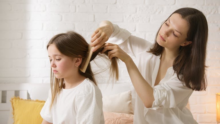 A mother carefully combs her daughter's hair in a warm and comfy indoor setting.