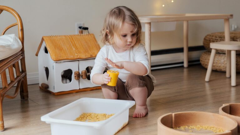 A young child playing with macaroni in a cozy indoor playroom setting.