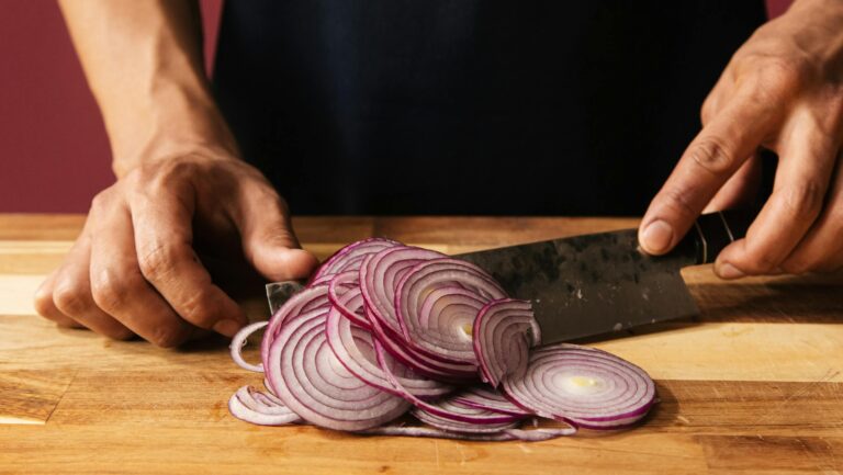 Close-up of hands slicing a red onion on a wooden chopping board, ideal for cooking content.