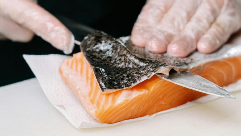 Close-up of salmon skin being removed by hands with a knife, showcasing food preparation.