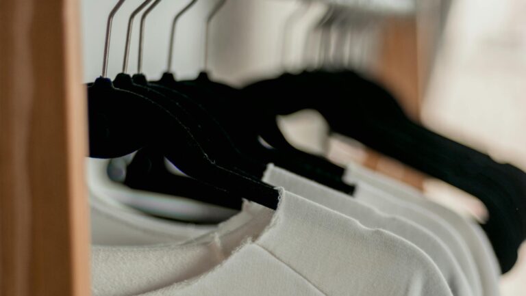 Close-up of white t-shirts hanging neatly on black hangers in a minimalist indoor closet setting.