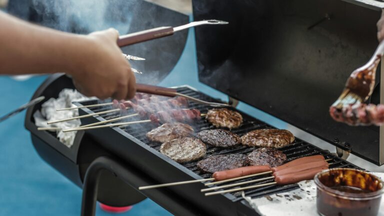 Delicious meats and sausages grilling on a barbecue outside, perfect for a summer picnic.