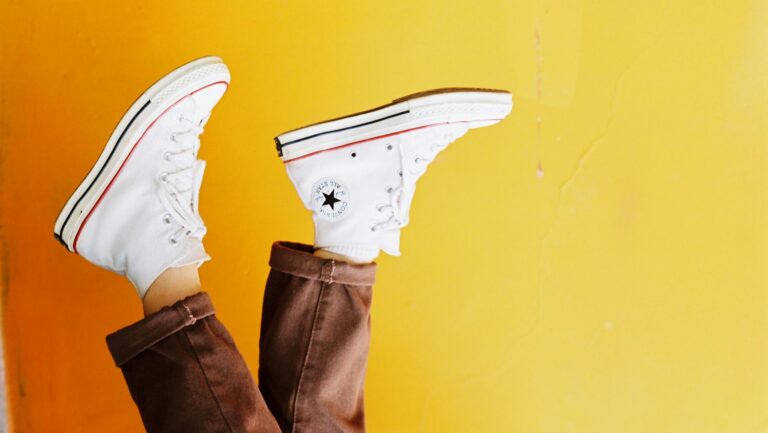 Upside down image of white sneakers against a vibrant yellow background, showcasing trendy footwear style.