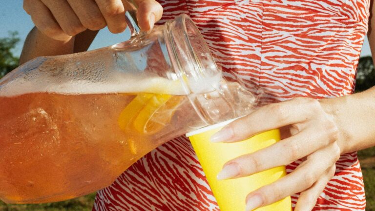 Woman pouring iced tea into a cup on a sunny picnic day outdoors.