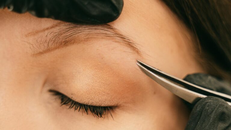 Zbliżenie na twarz kobiety podczas regulacji brwi pęsetą