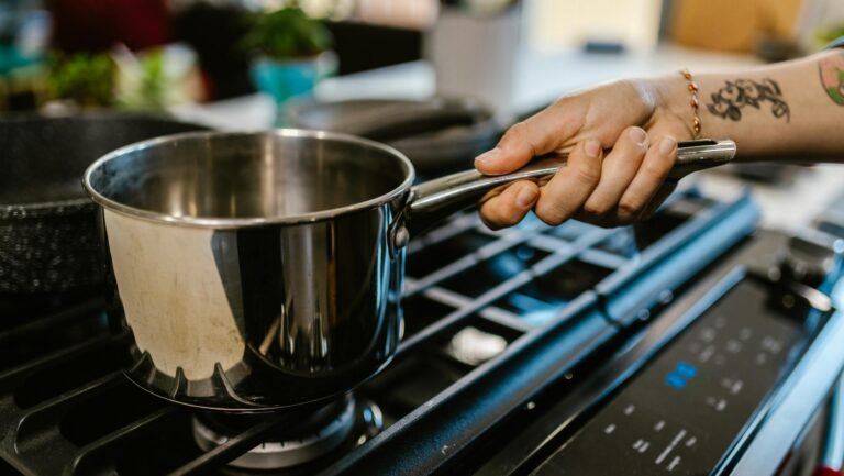 Stalowy rondelek na kuchence gazowej trzymany za rączkę
