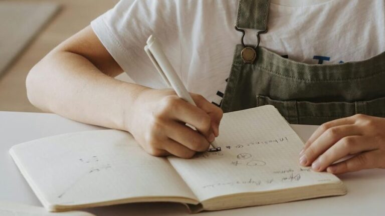 Przybliżenie na dziewczynkę piszącą długopisem w zeszycie