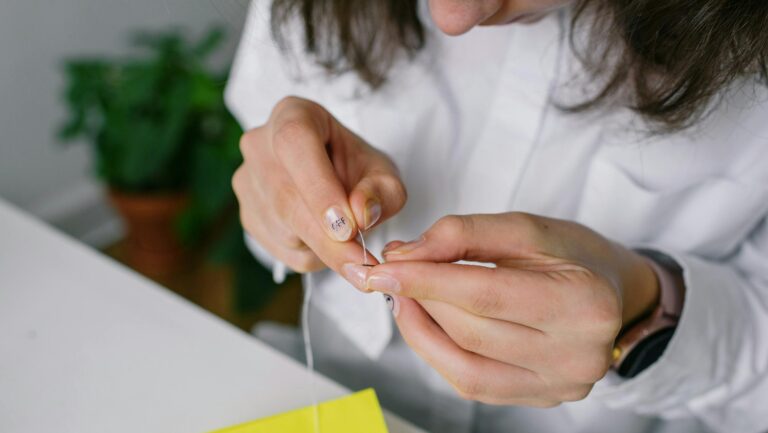 Detailed shot of a woman threading a needle with a blurred background.