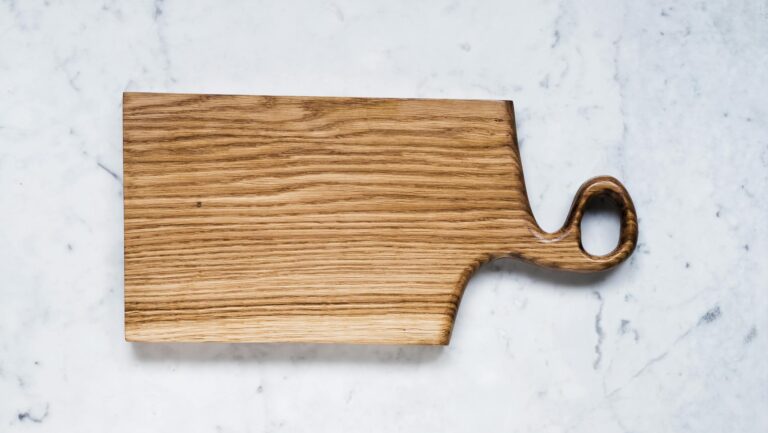 Vertical wooden cutting board with handle on marble background, ideal for culinary use.