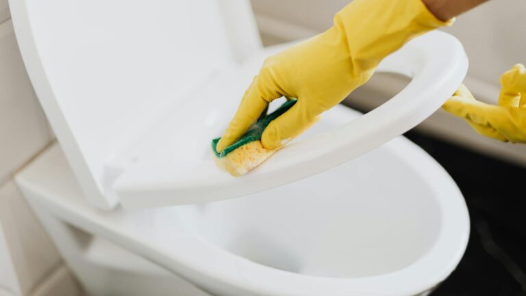 Osoba myjąca toaletę w żółtych rękawiczkach