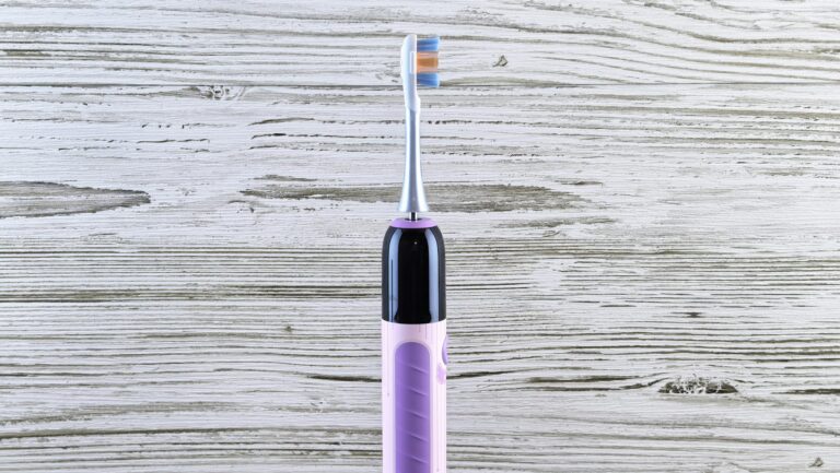 Elektryczna szczoteczka do zębów, stojąca na tle drewnianej ściany