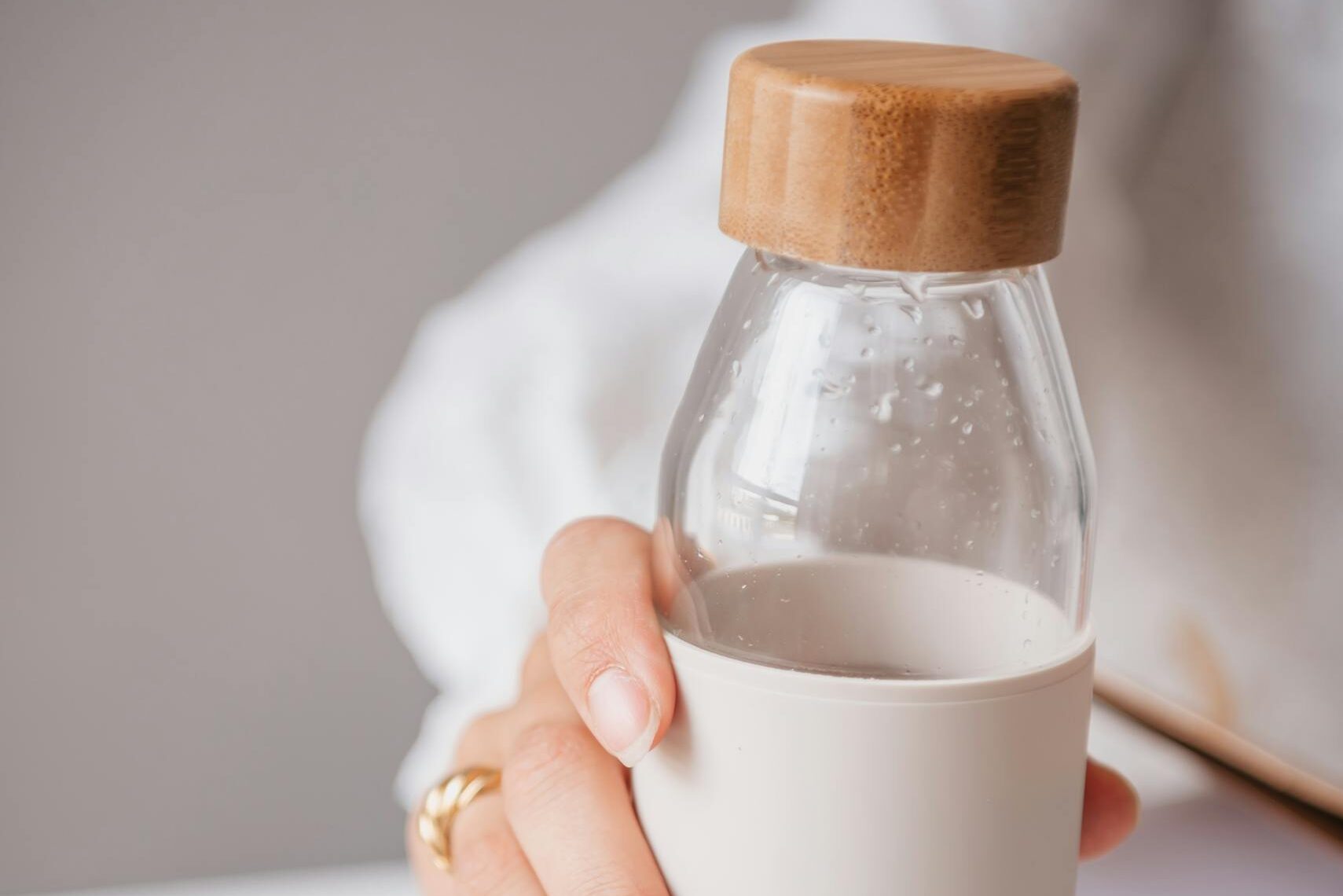 Zbliżenie na rękę kobiety trzymającą szklaną butelkę z drewnianą nakrętką i sylikonową osłonką