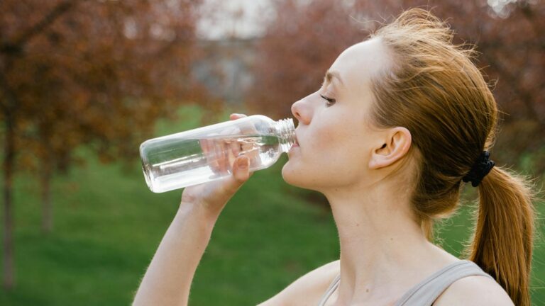 Kobieta w sportowym stroju, pijąca wodę z butelki wielokrotnego użytku na zewnątrz