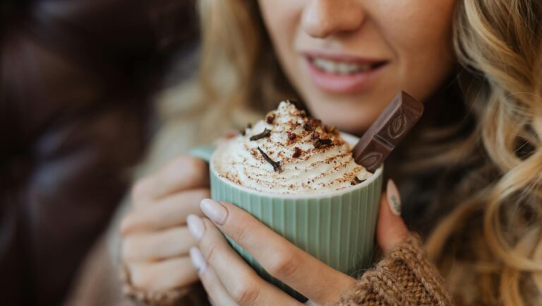 Kobieta trzymająca kubek gorącej czekolady z bitą śmietaną i dodatkami