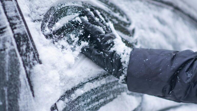 Zbliżenie na rękę zdejmującą śnieg z szyby w samochodzie