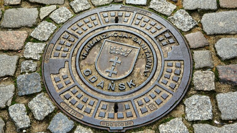Pokrywa studzienki kanalizacyjnej w Gdańsku otoczona kostką brukową