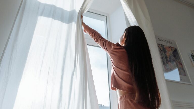 Kobieta odsłaniająca zasłony w celu otworzenia okna i przewietrzenia mieszkania