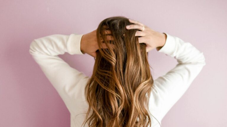 Stojąca tyłem kobieta, która trzyma ręce w swoich długich ciemnych włosach